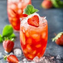glass of pink liquid and ice cubes garnished with strawberries and a mint sprig